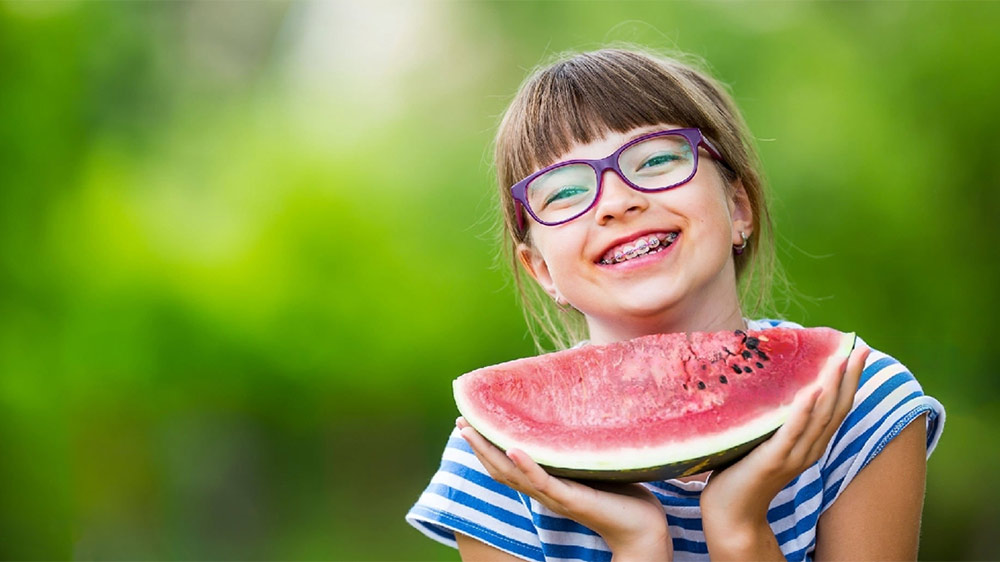 smiling girl with orthodontics is holding a slice of watermelon