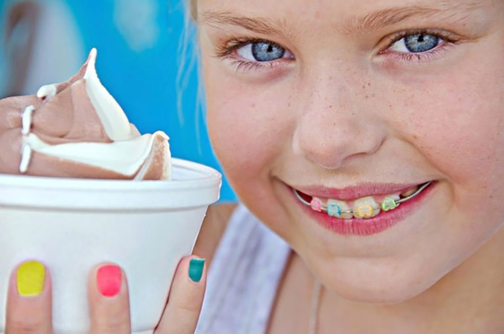 a little girl with colored orthodontics and ice cream and colored lacquer