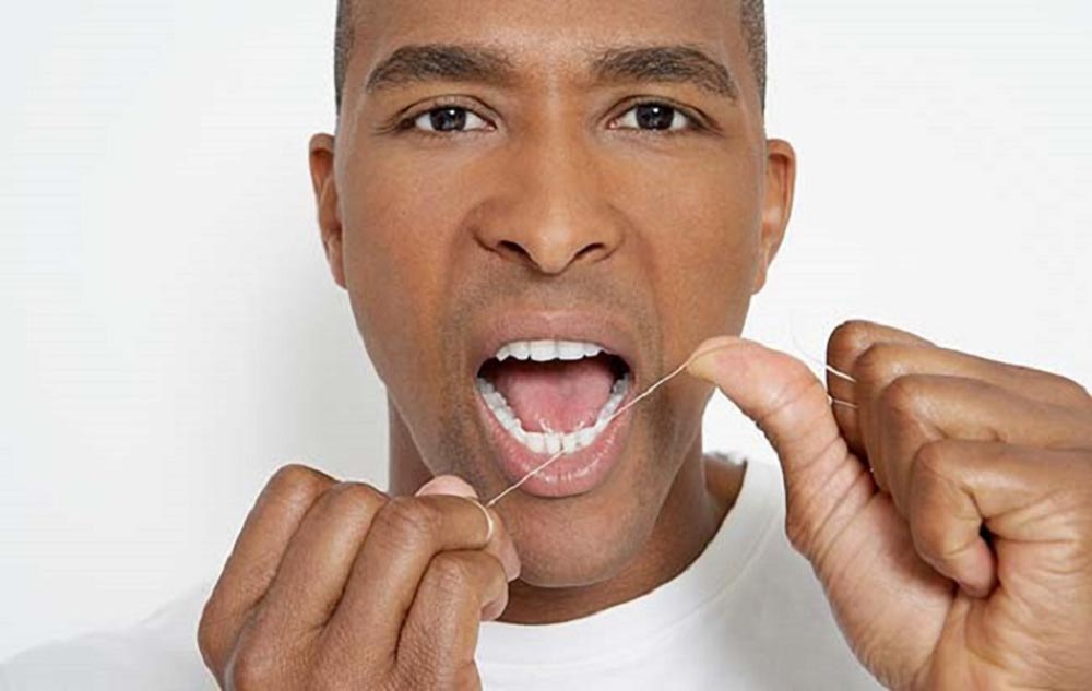 یک مرد سیاه پوست با دندان های مرتب که در حال نخ دندان کشیدن است