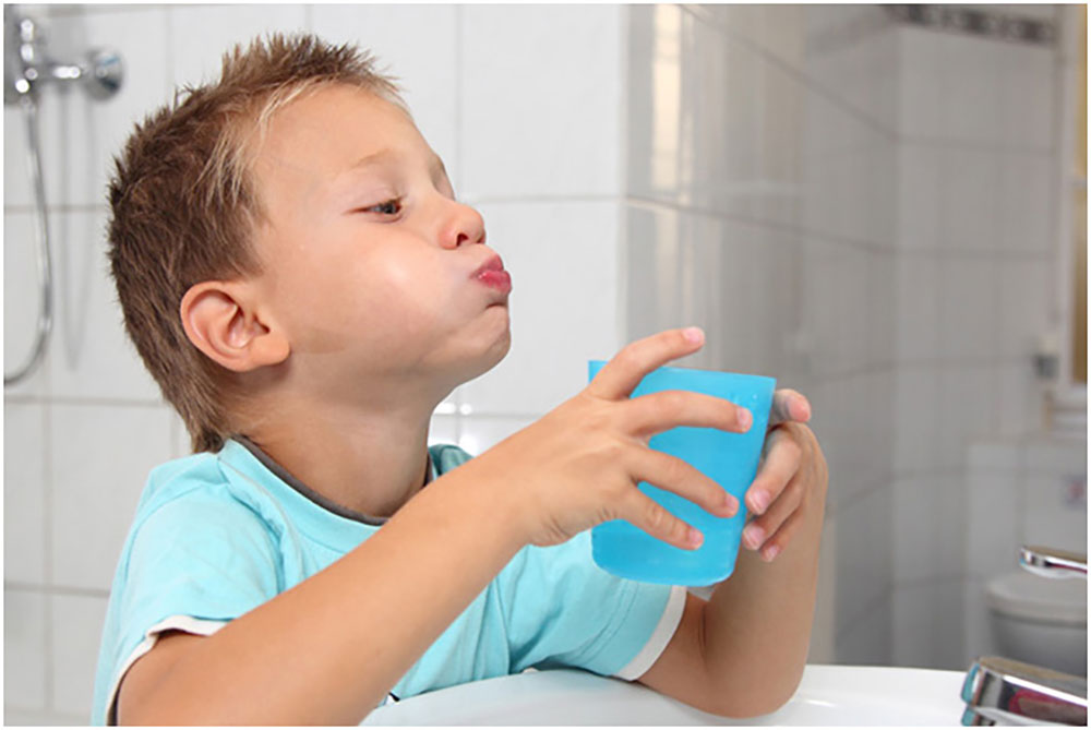 a boy with a glass in his hand, gargling mouthwash
