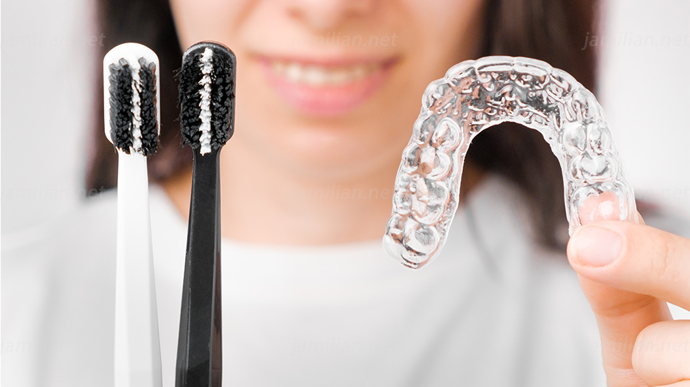 a woman holding two toothbrushes and a removable retainer