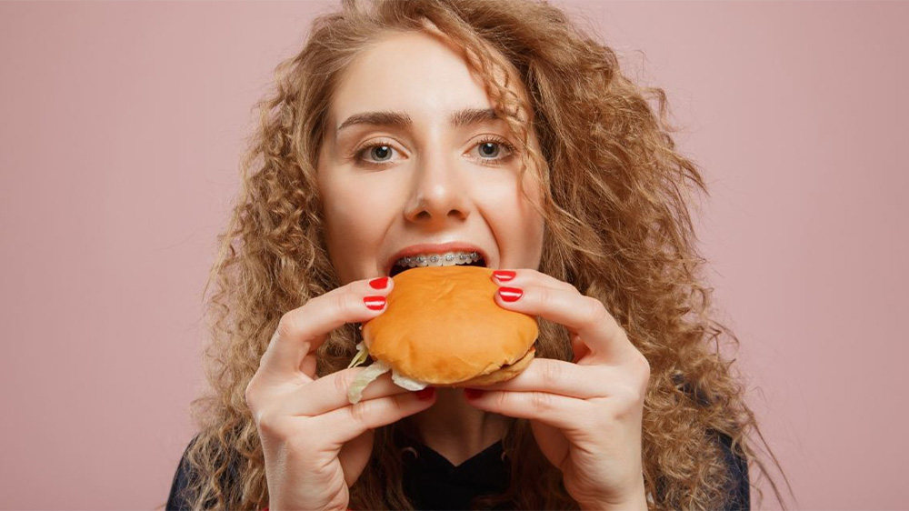 دختر جوان با دندان های ارتودنسی شده در حال گاز زدن همبرگر