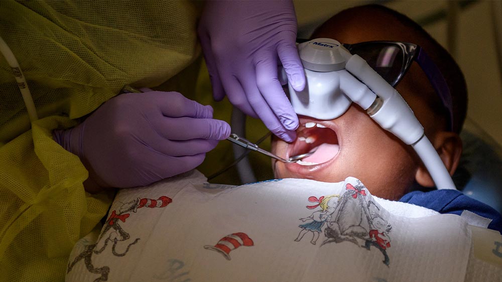 دندانپزشک با استفاده از بیهوشی در حال بررسی دندان کودک