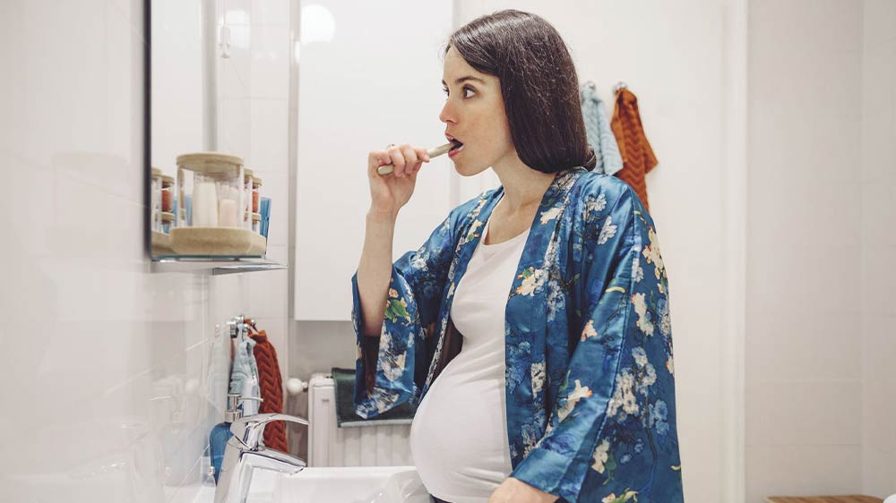 pregnant woman in her pajamas brushing her teeth