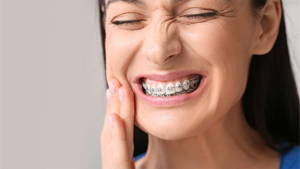 Frau mit kieferorthopädischer Behandlung leidet unter Schmerzen im Mund