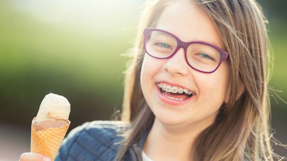 دختری با عینک و دندان ارتودنسی شده در حال خوردن بستنی